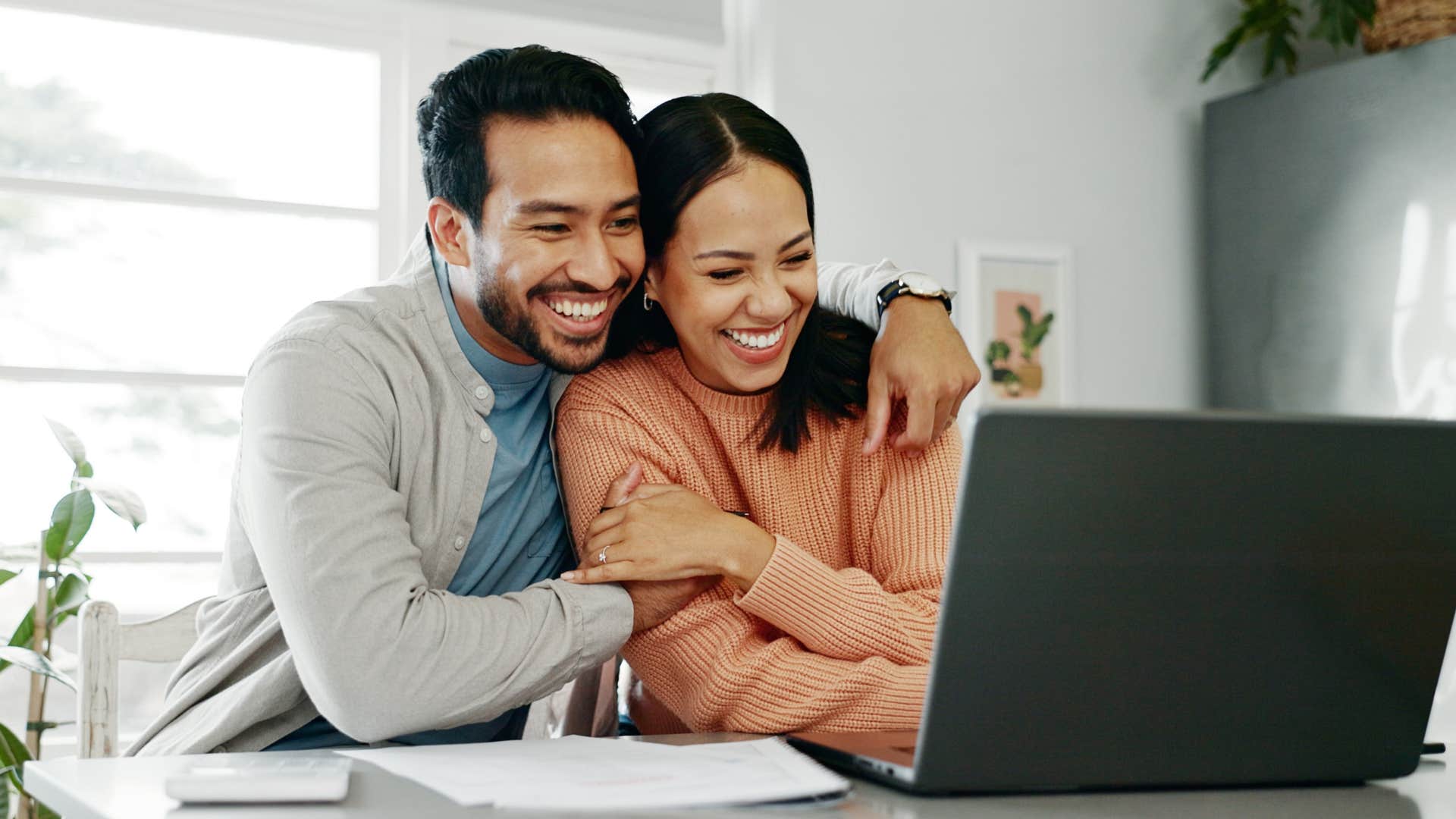 Happy married couple hugging while looking at their laptop.