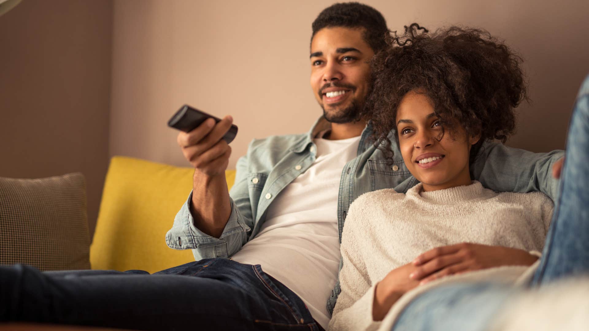 Couple smiling and watching TV together.