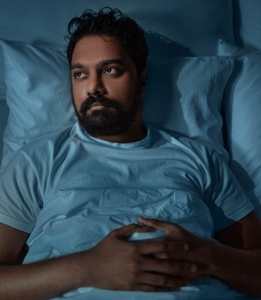 Man lays in bed with hands on stomach thinking