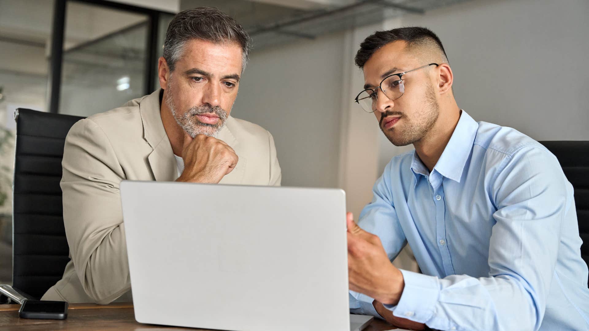 Two men looking serious staring at a laptop. 