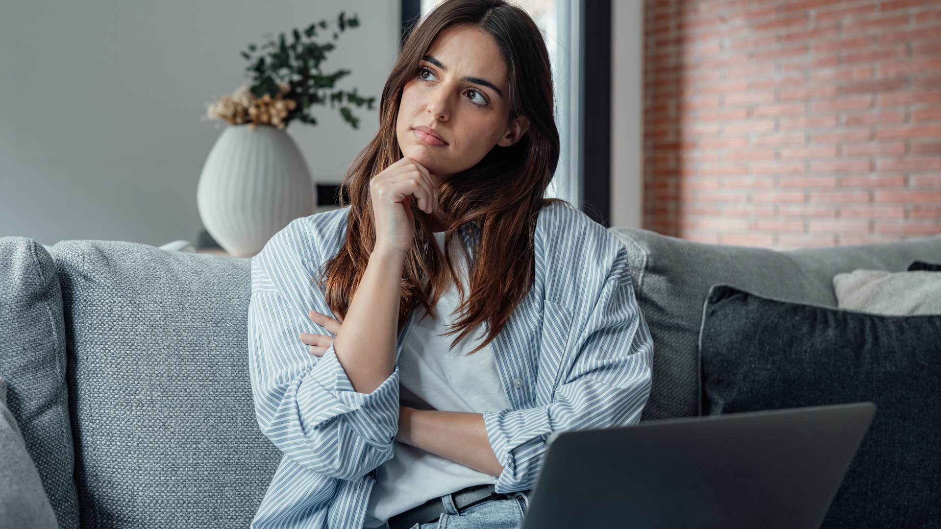 Woman thinking with her laptop in her lap. 