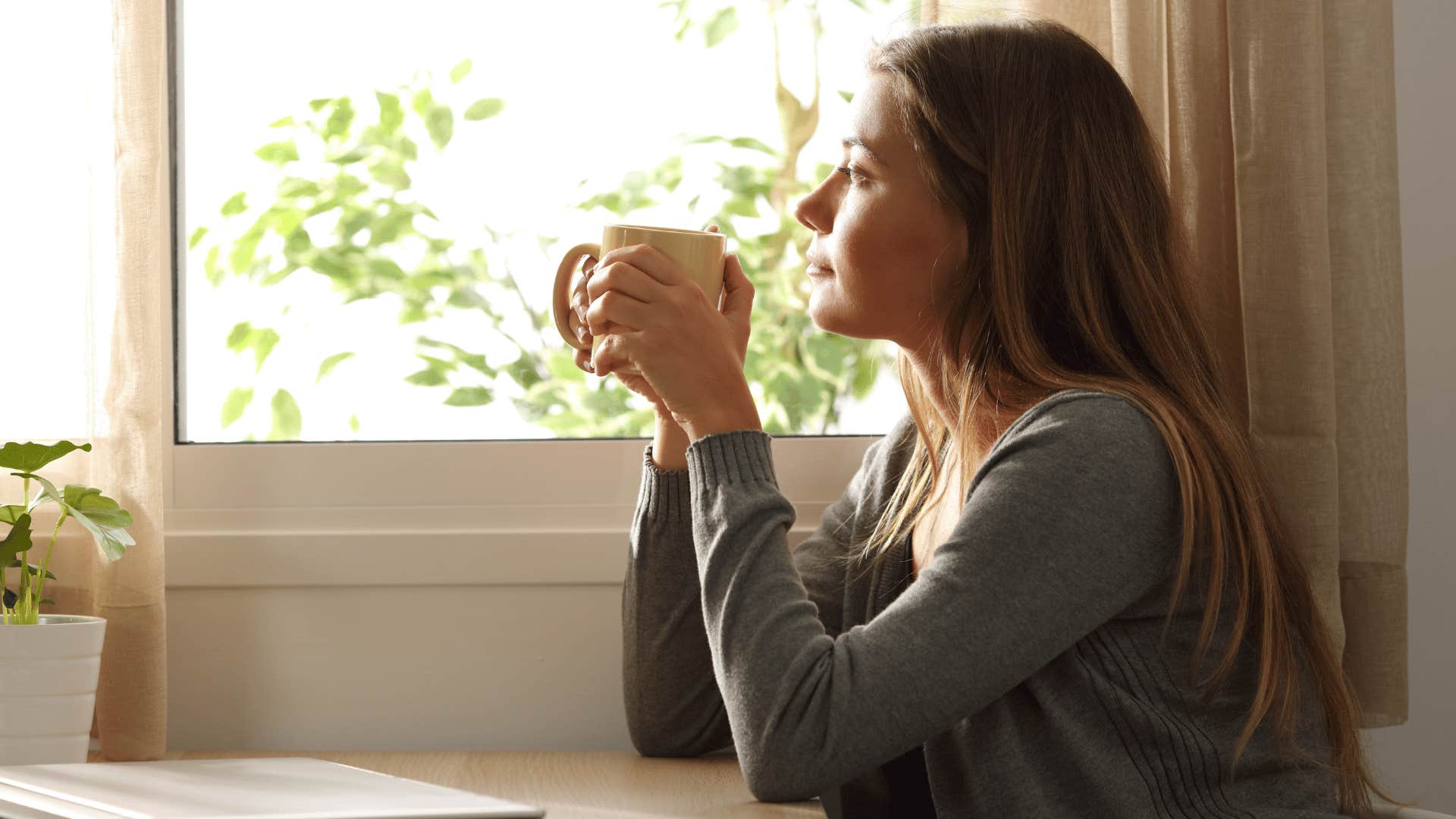 woman drinking hot drink and looking out the window