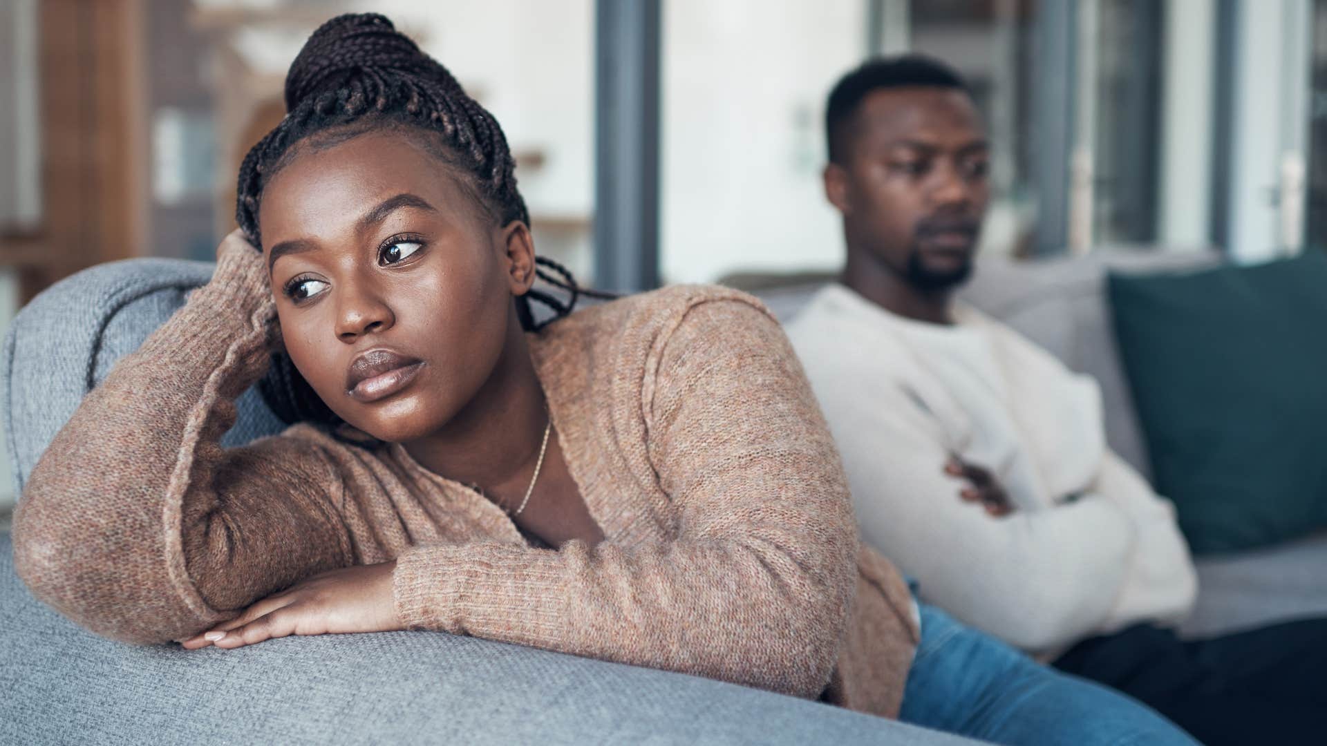 Woman looking upset sitting next to her partner on the couch.