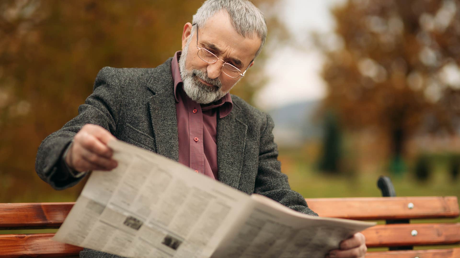 Older man reading a newspaper on a bench