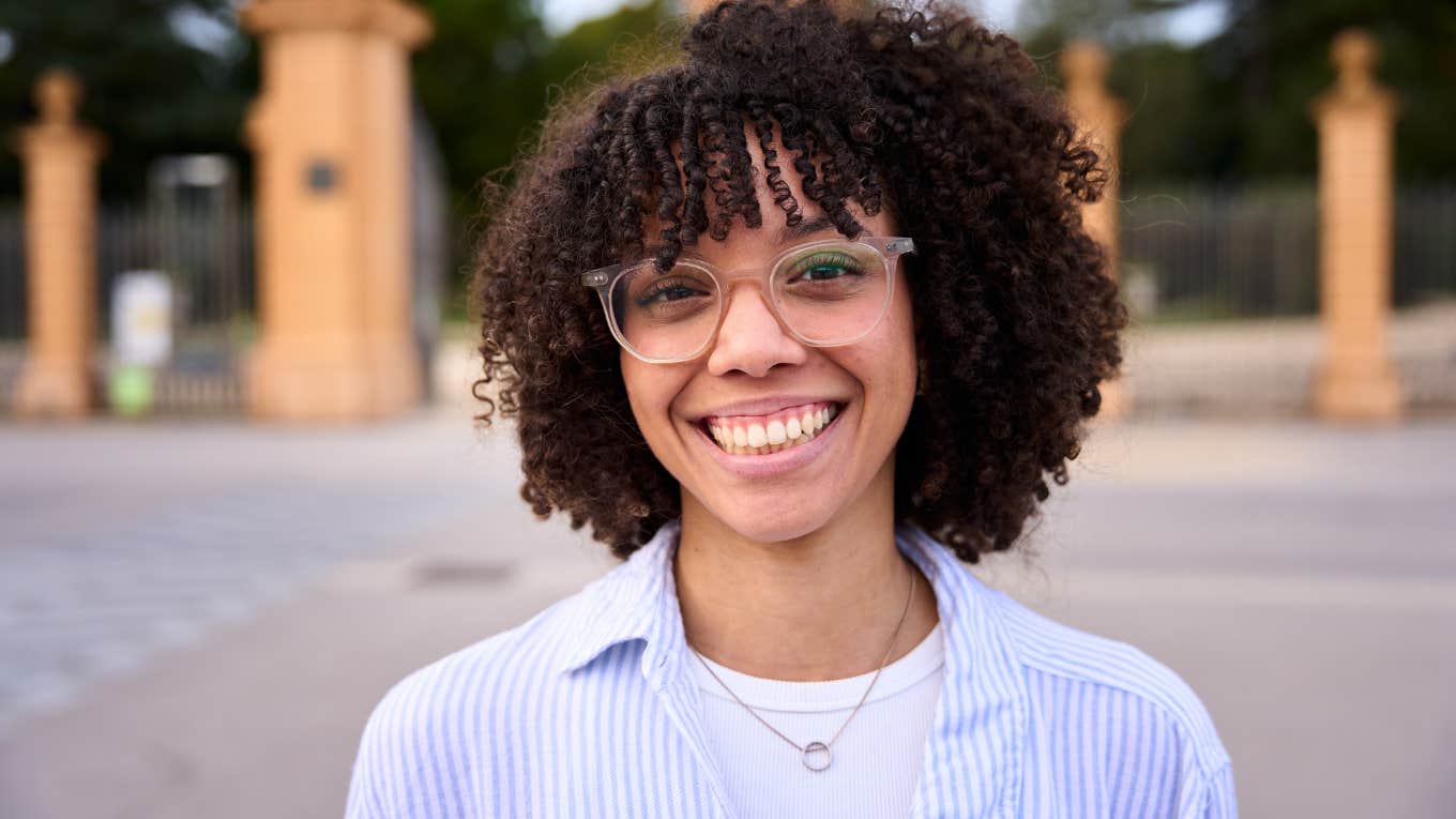 Gen Z woman smiling outside at the camera.