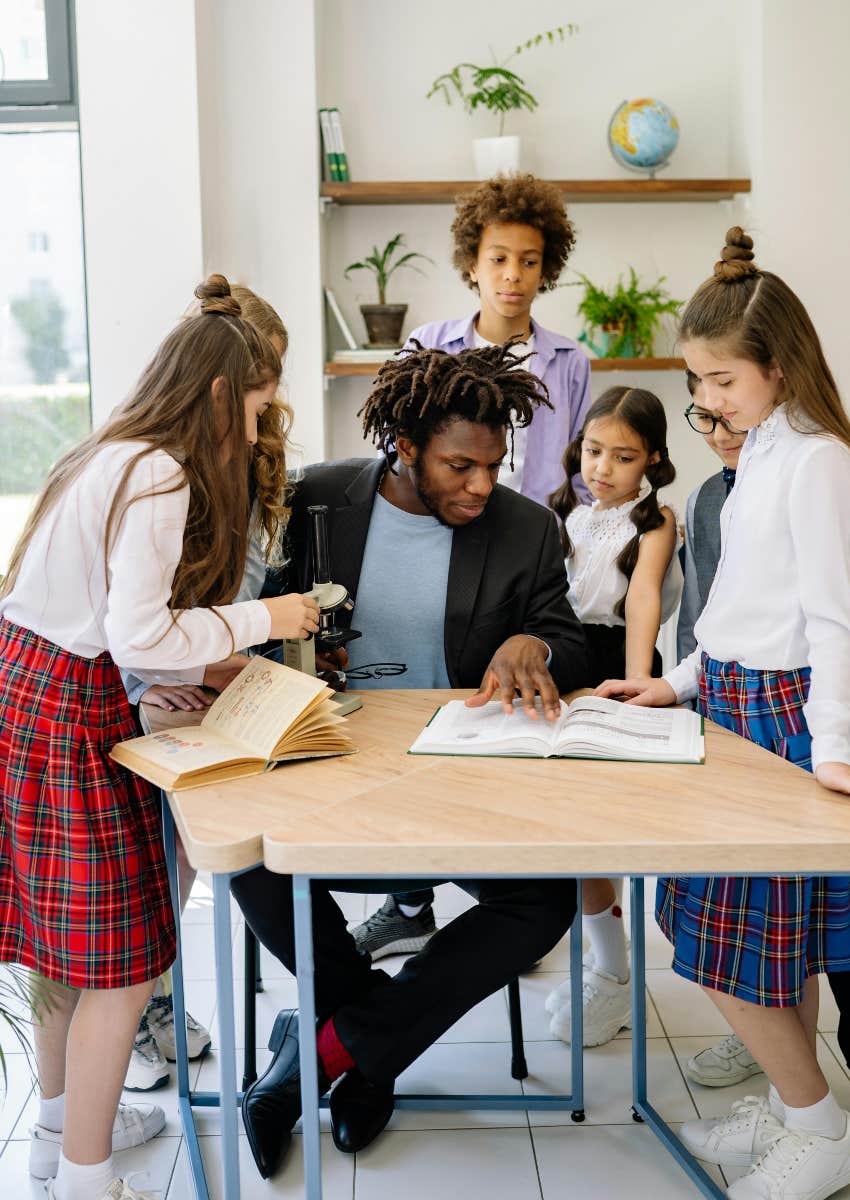 teacher and students looking at a book on a desk