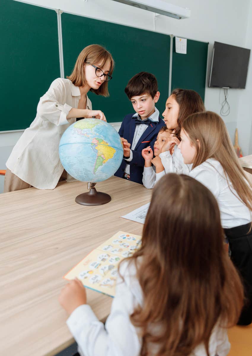 teacher and students looking at globe on desk in classroom