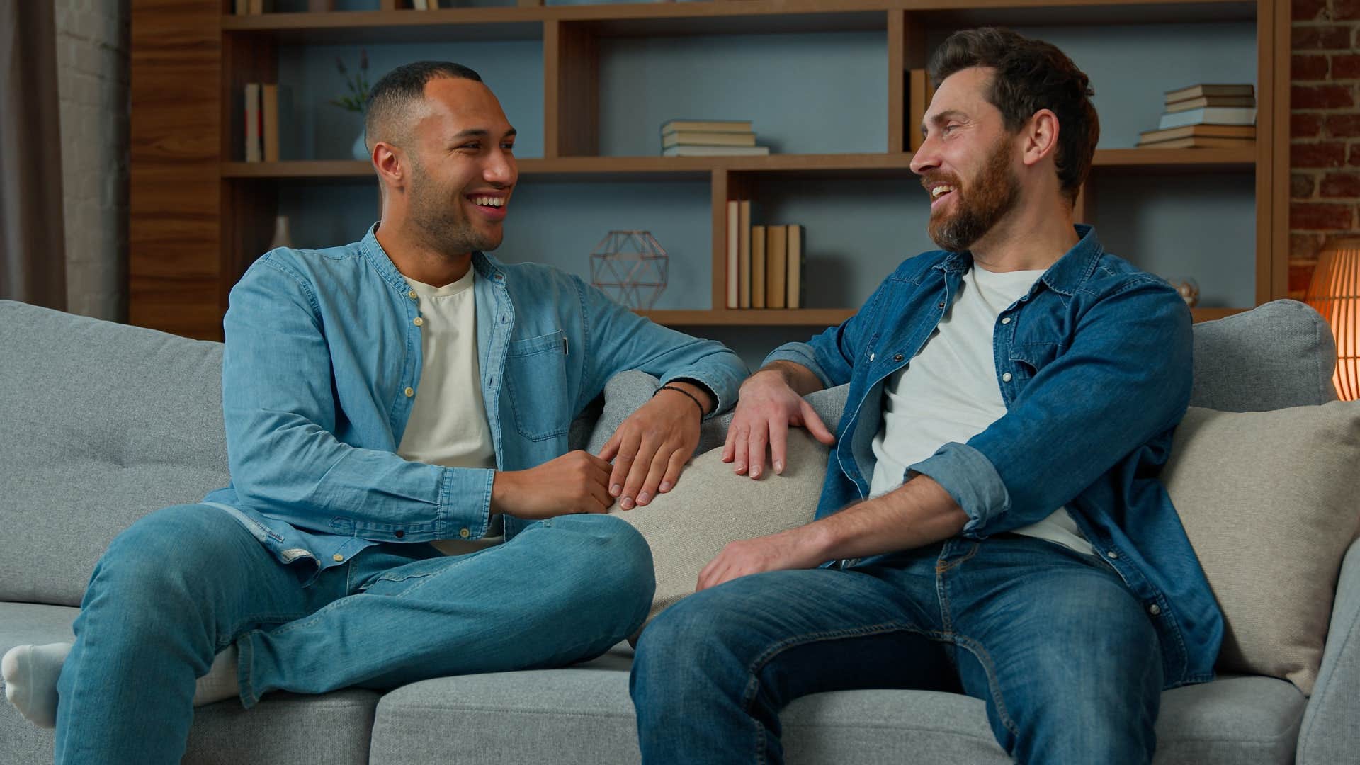 Two men sitting on a couch talking together.