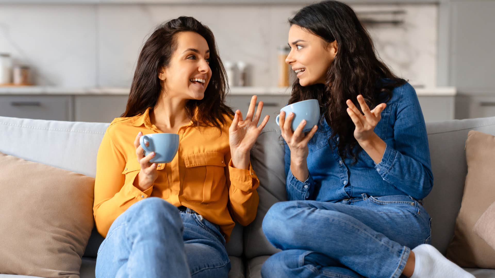 Two women smiling and talking together on a couch.