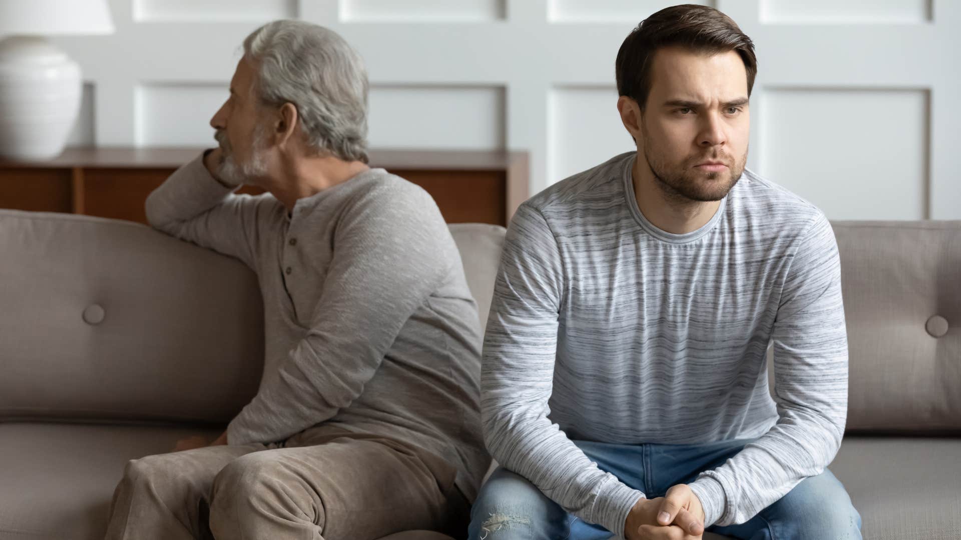 Adult son turned away from his upset father on the couch.