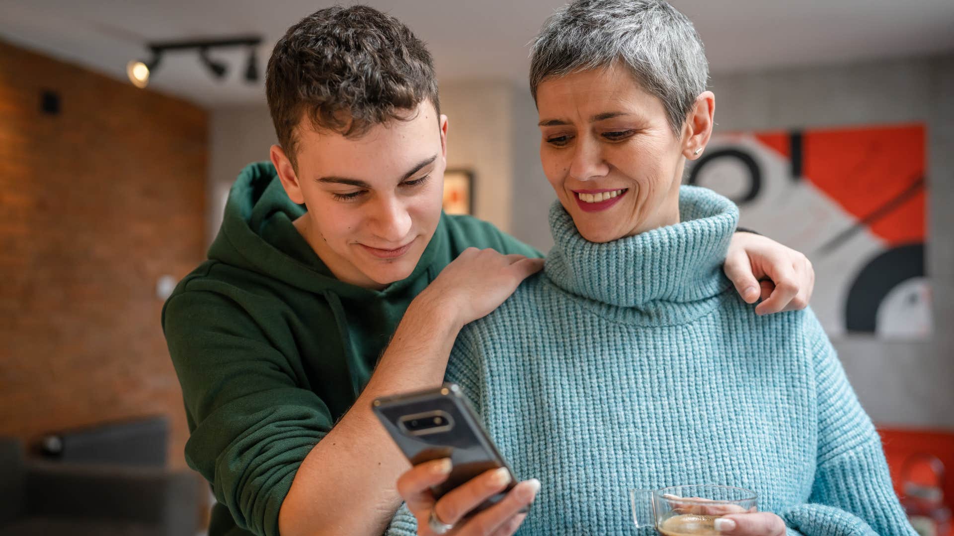 Gen X woman smiling at her phone next to her son