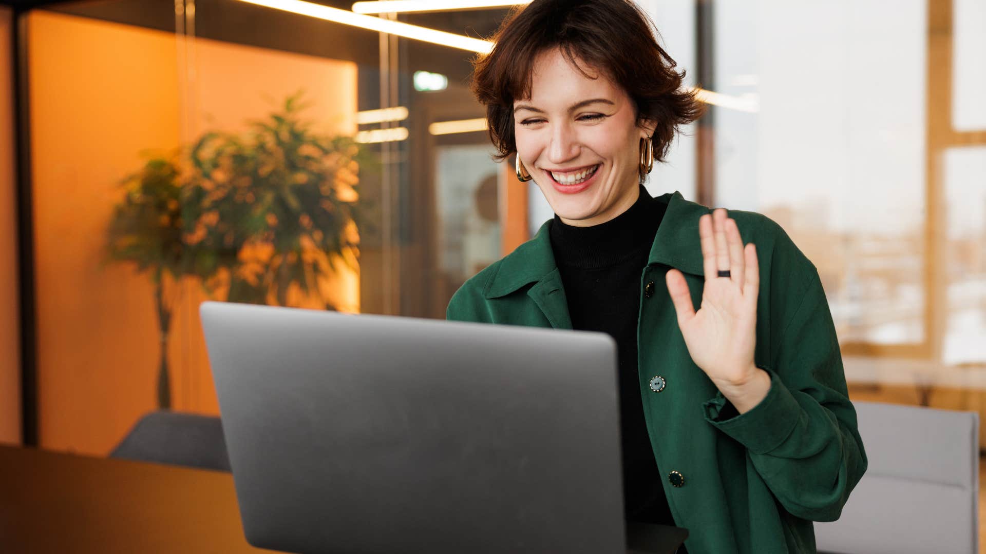 Gen Z woman smiling and waving to her laptop.