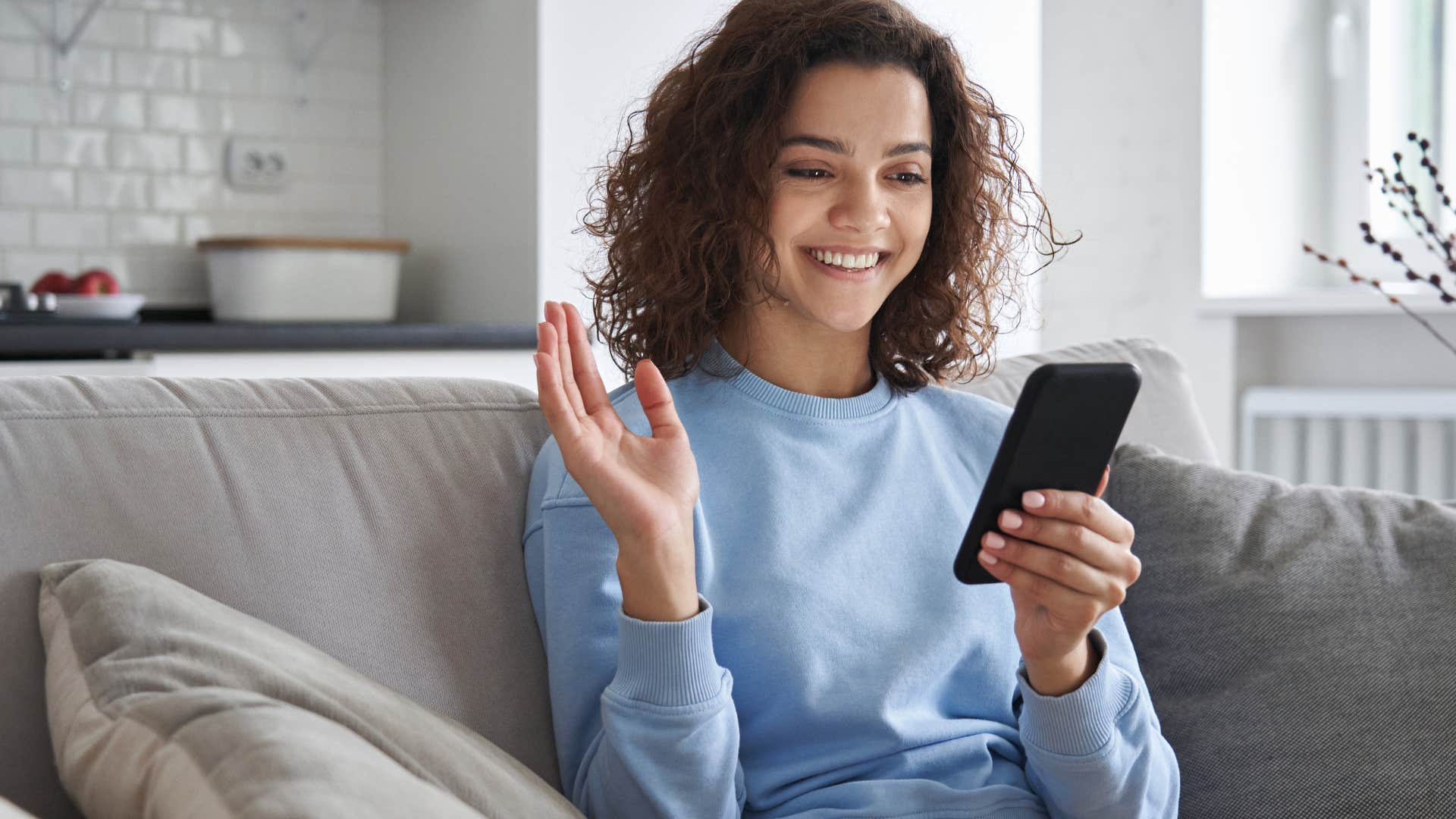 Woman smiling at her cell phone on the couch.