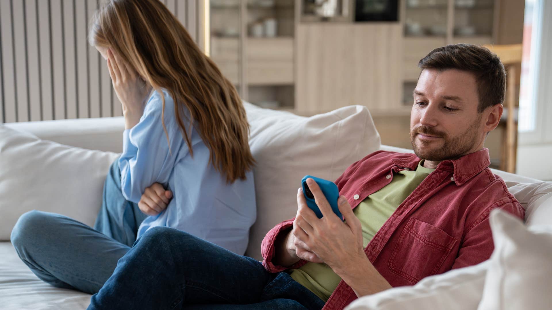 Man smiling at his phone while a woman looks upset behind him.