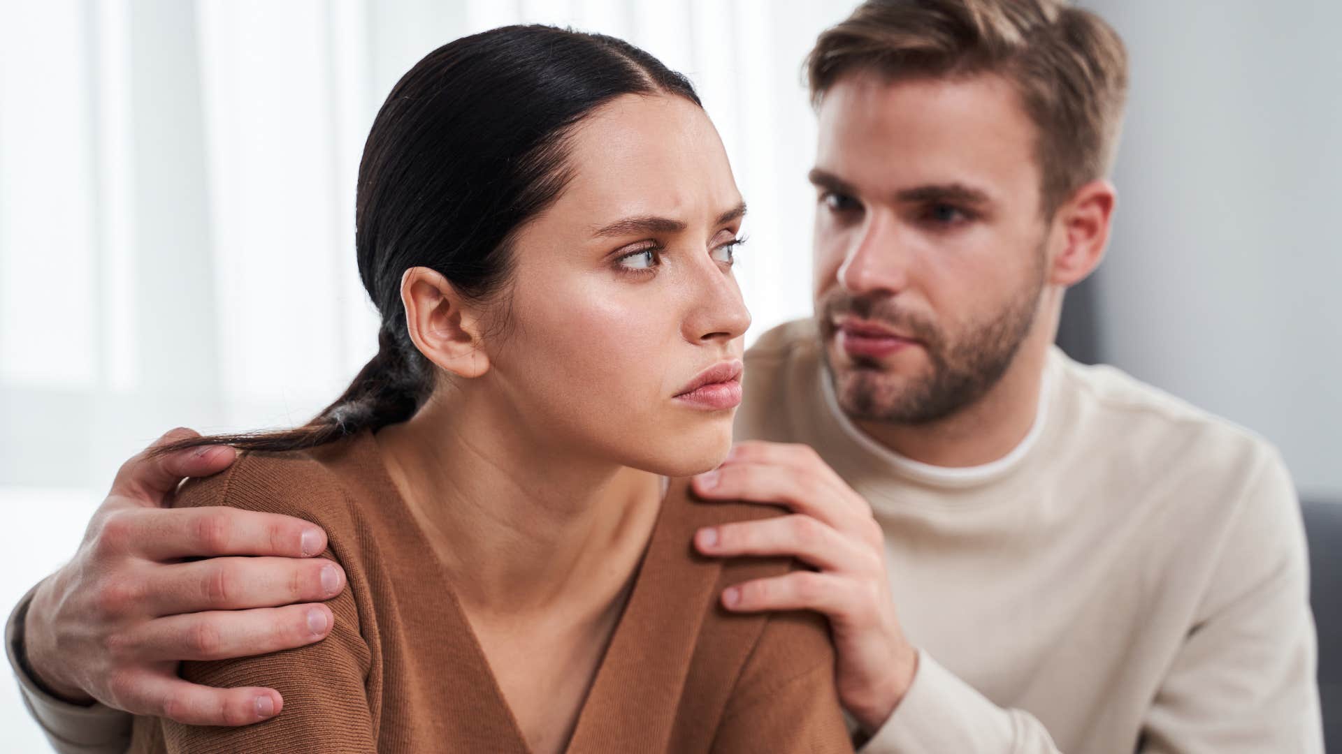 Woman looking annoyed while her husband comforts her.