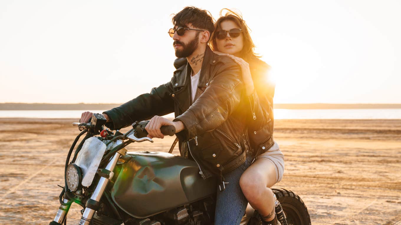 husband and wife riding motorcycle on the beach looking off into the distance