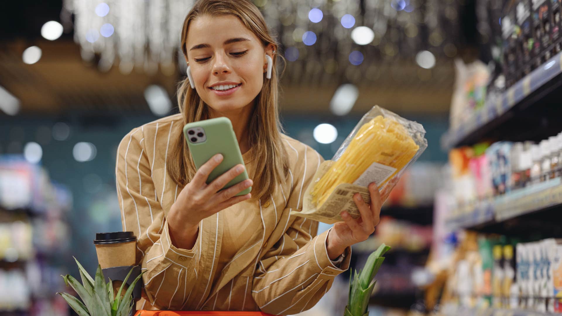 Woman holding bread and texting in a grocery store.