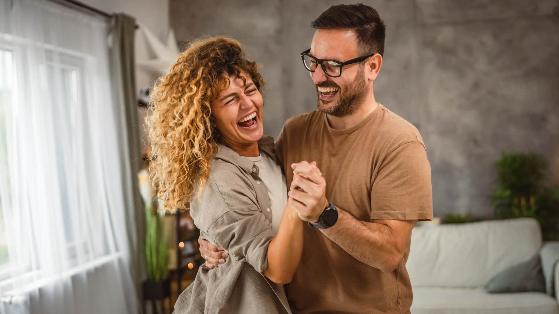 Woman smiling while dancing with a man at home.