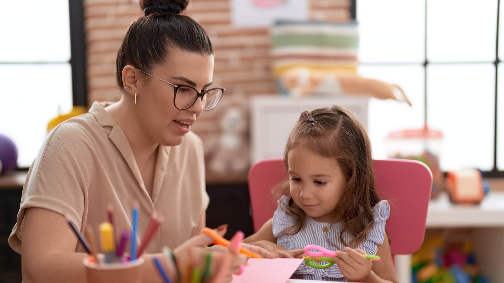 Teacher cutting paper next to her young student