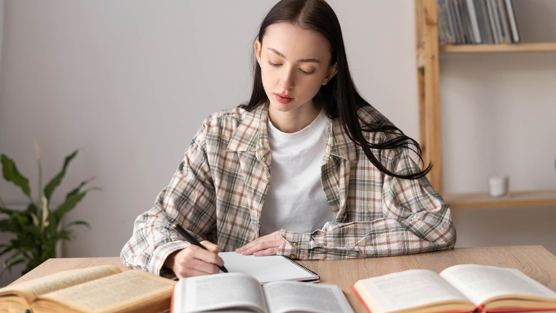 Young woman writing on her desk surrounding by textbooks