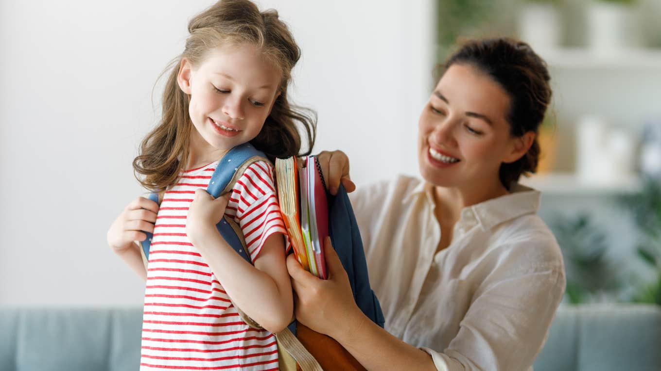 Mom packing her smiling daughter's backpack for school. 