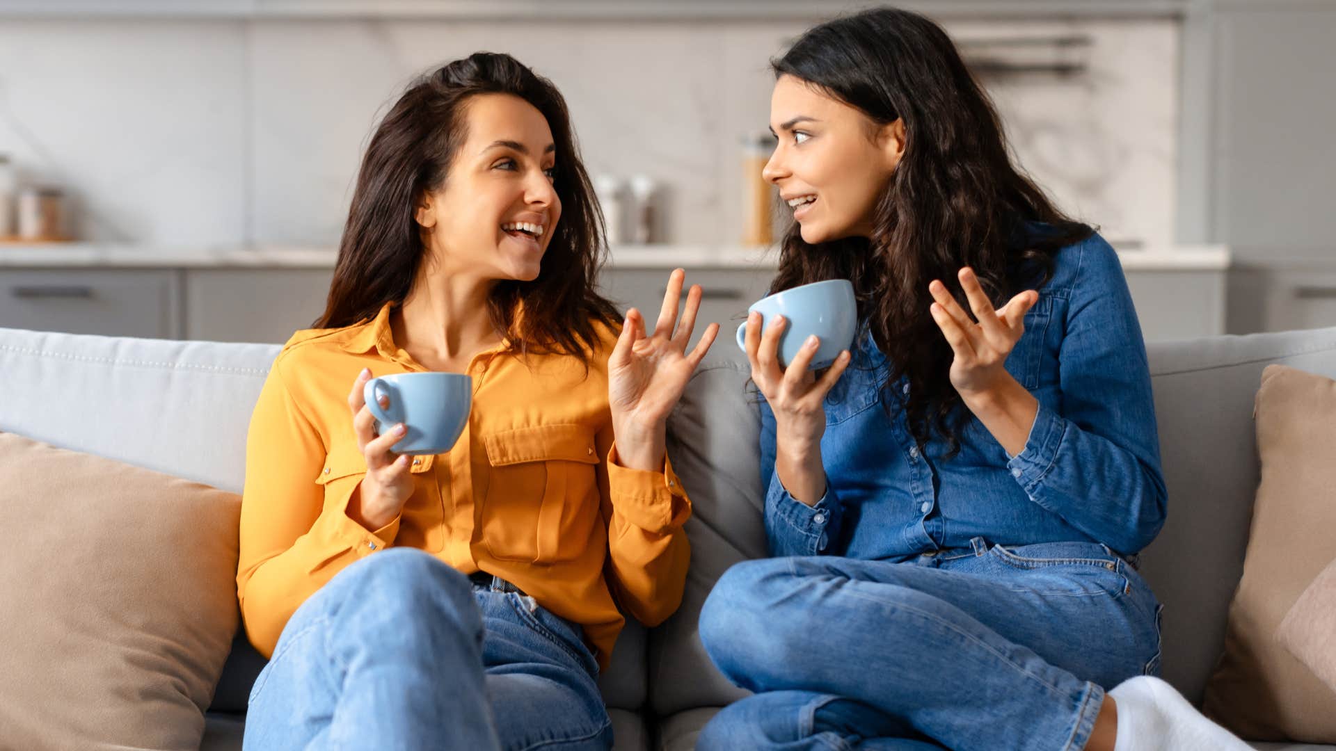 Two women gossiping together on a couch.