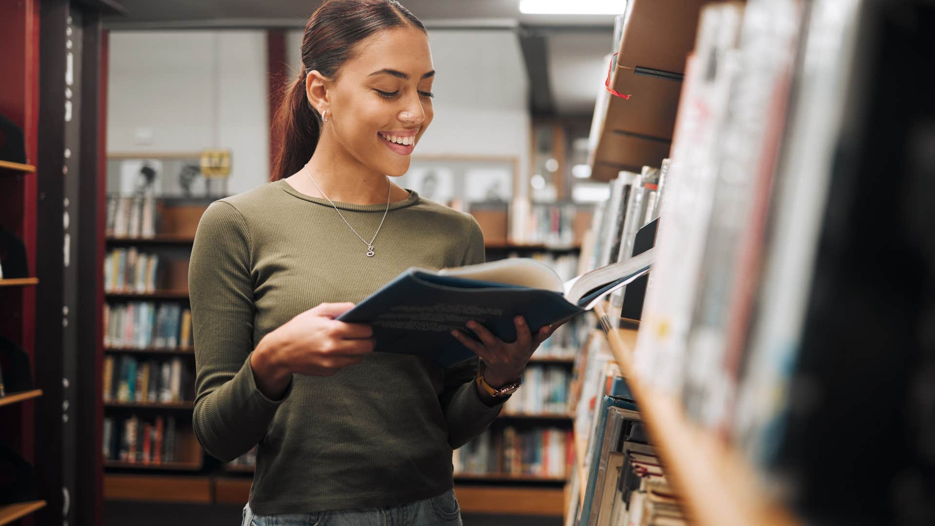 Woman smiling and reading a book in the library.