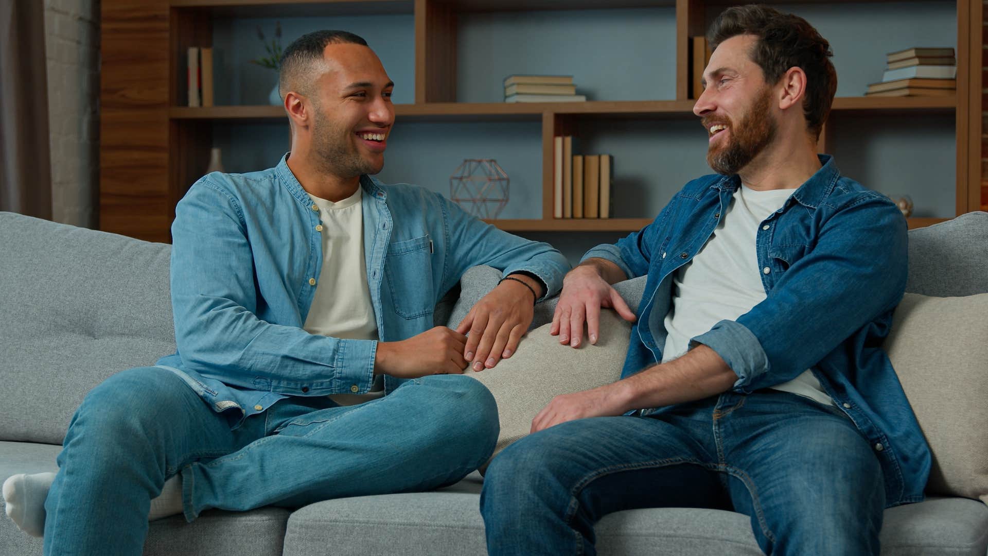 Two men talking and smiling together on a couch.