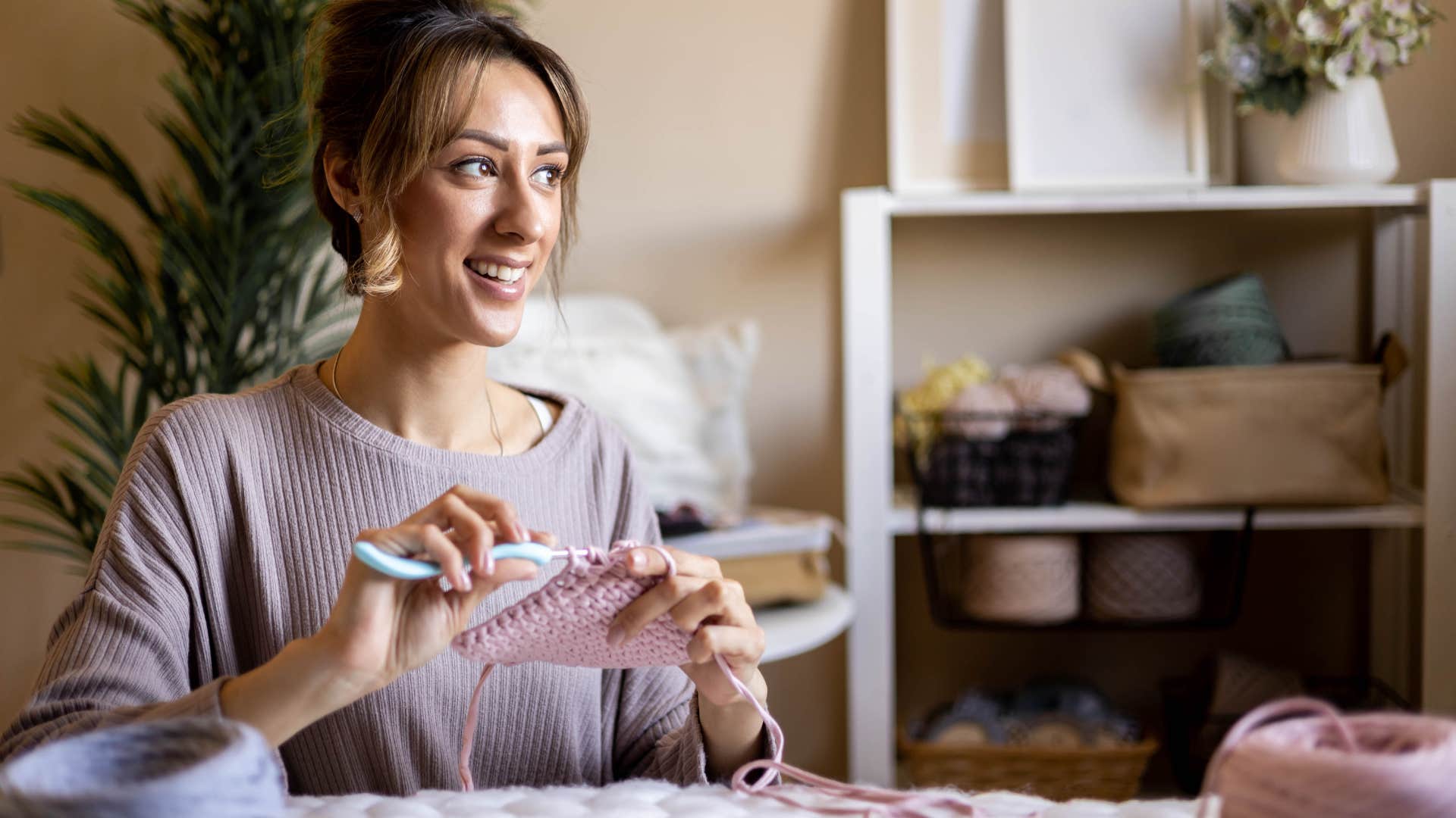 Woman smiling and crocheting at a table. 