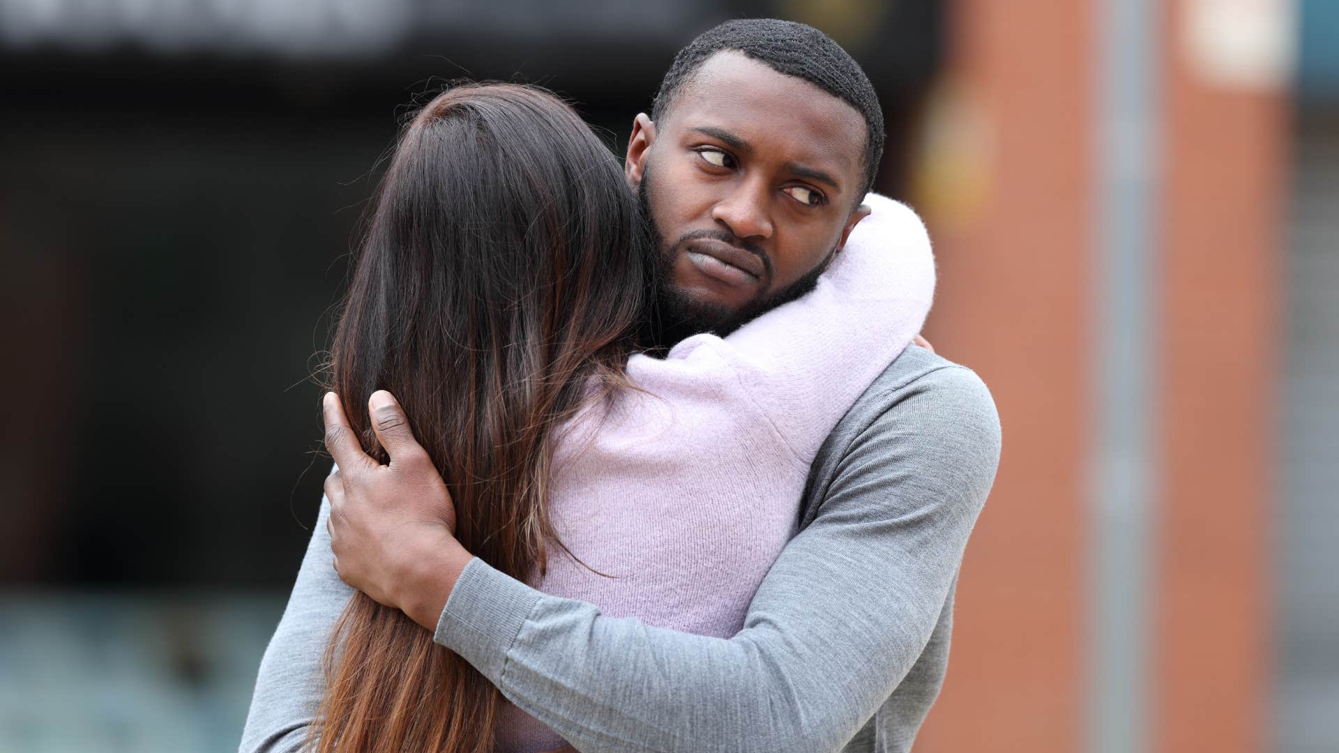 emotionally stunted man looking annoyed while hugging a woman