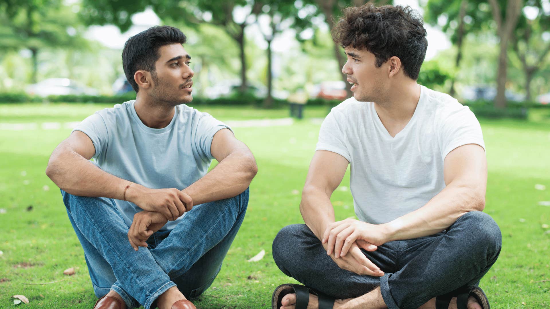 two men talking while sitting on grass