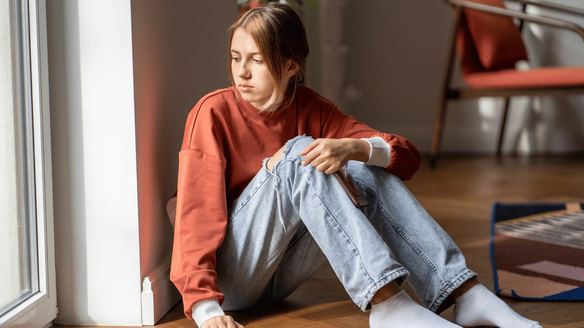 young woman looking out of window while sitting on the floor 