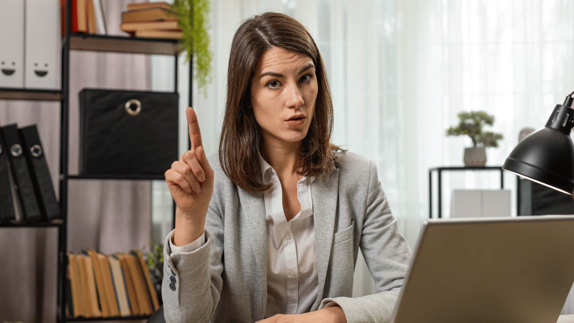 She sits behind a desk and raises her index finger