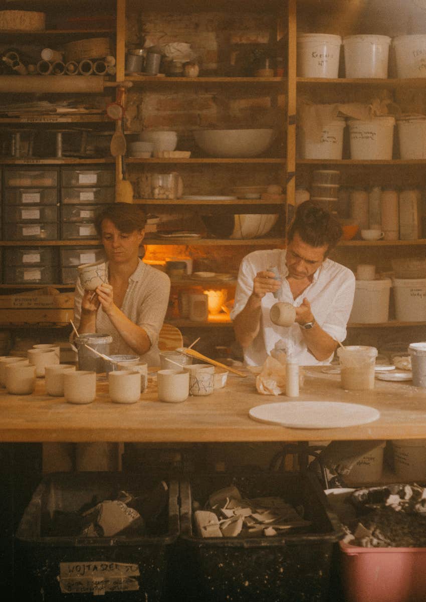 two people sitting together and painting ceramic cups