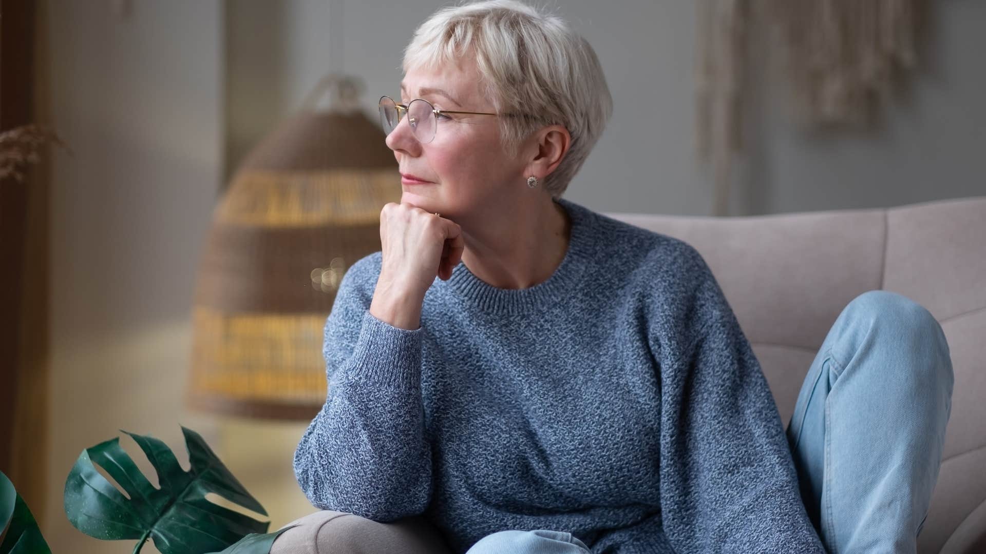 Older woman looking reflective staring out a window