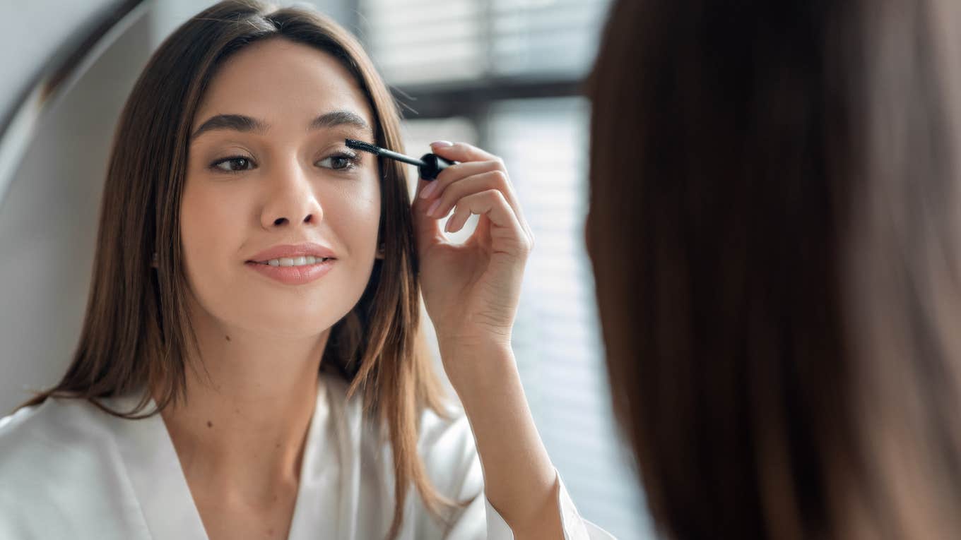 woman looking in mirror putting on mascara