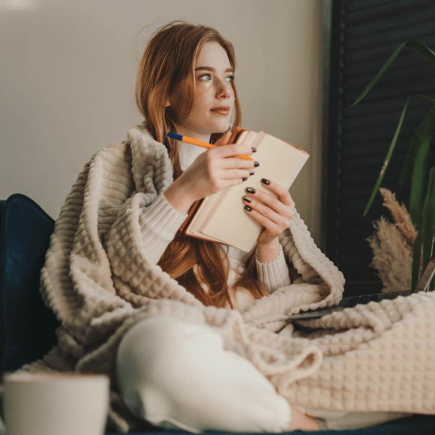 woman wrapped in a blanket holding an open notebook