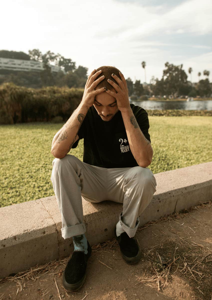 young man anxiously holding his head outside