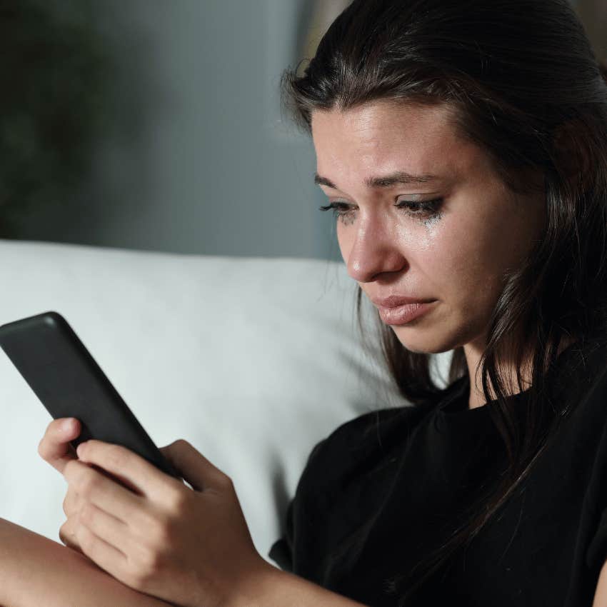 young woman crying while staring at her phone