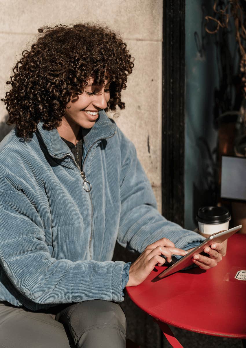 young woman with curly hair smiling down at tablet