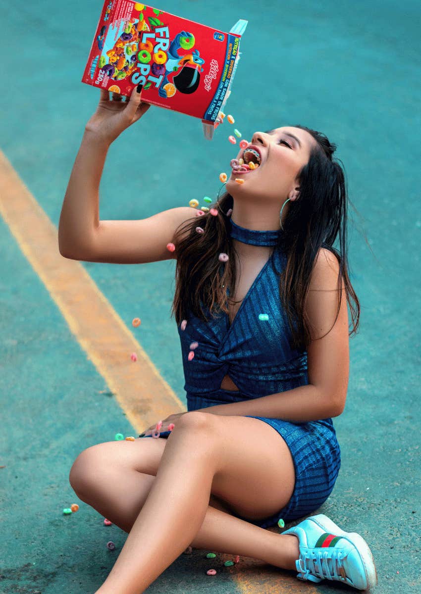 young woman pouring a box of fruit loops into her mouth