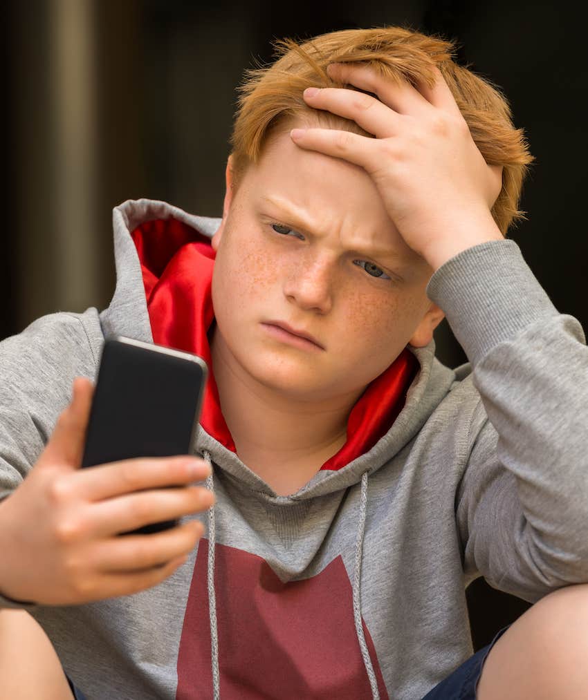 Anxious teen looks at mobile phone and is challenged