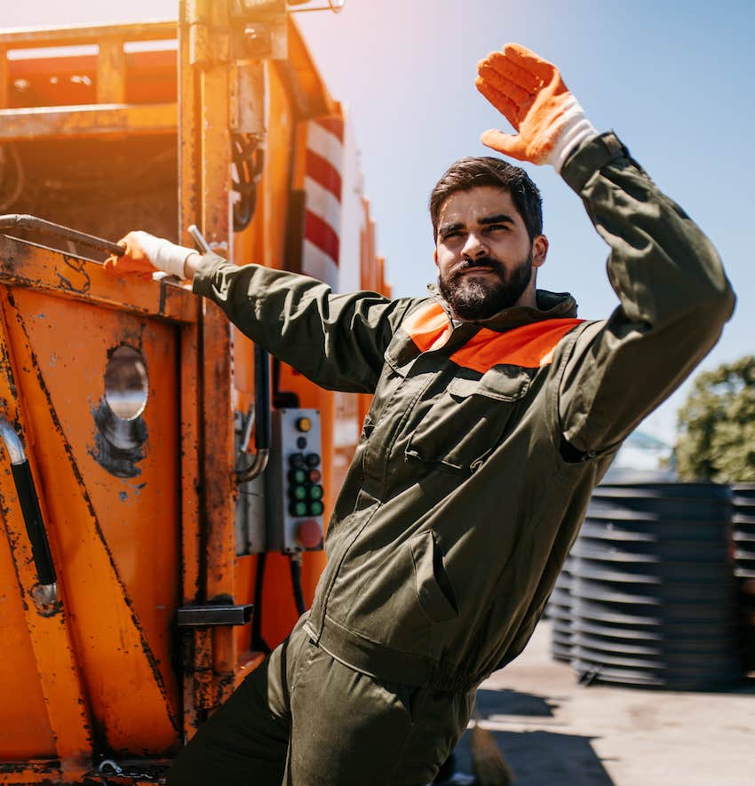 Bearded garbage man rides the back of truck