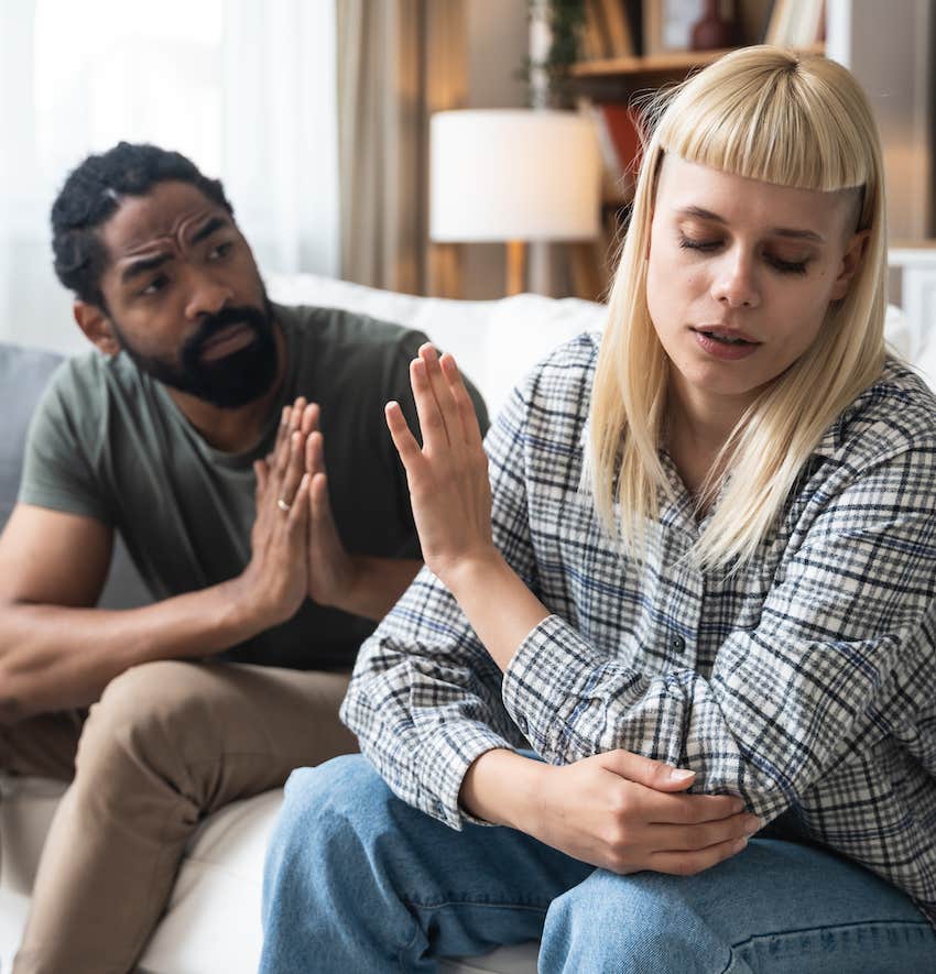 Self-critical woman holds hand up and rejects apologetic man