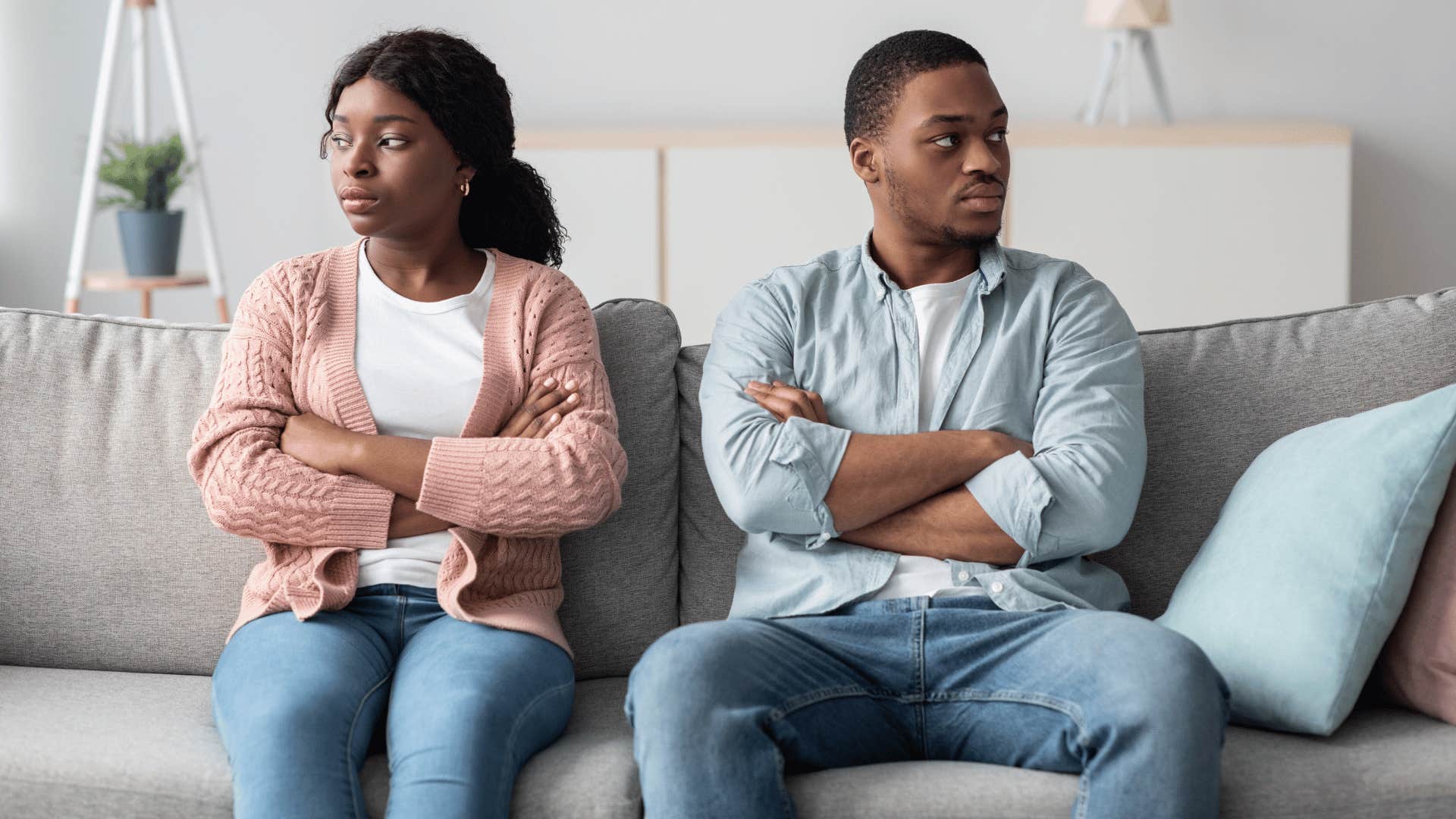 Couple lacking emotional intimacy sit on a couch and cross arms while looking away from each other 