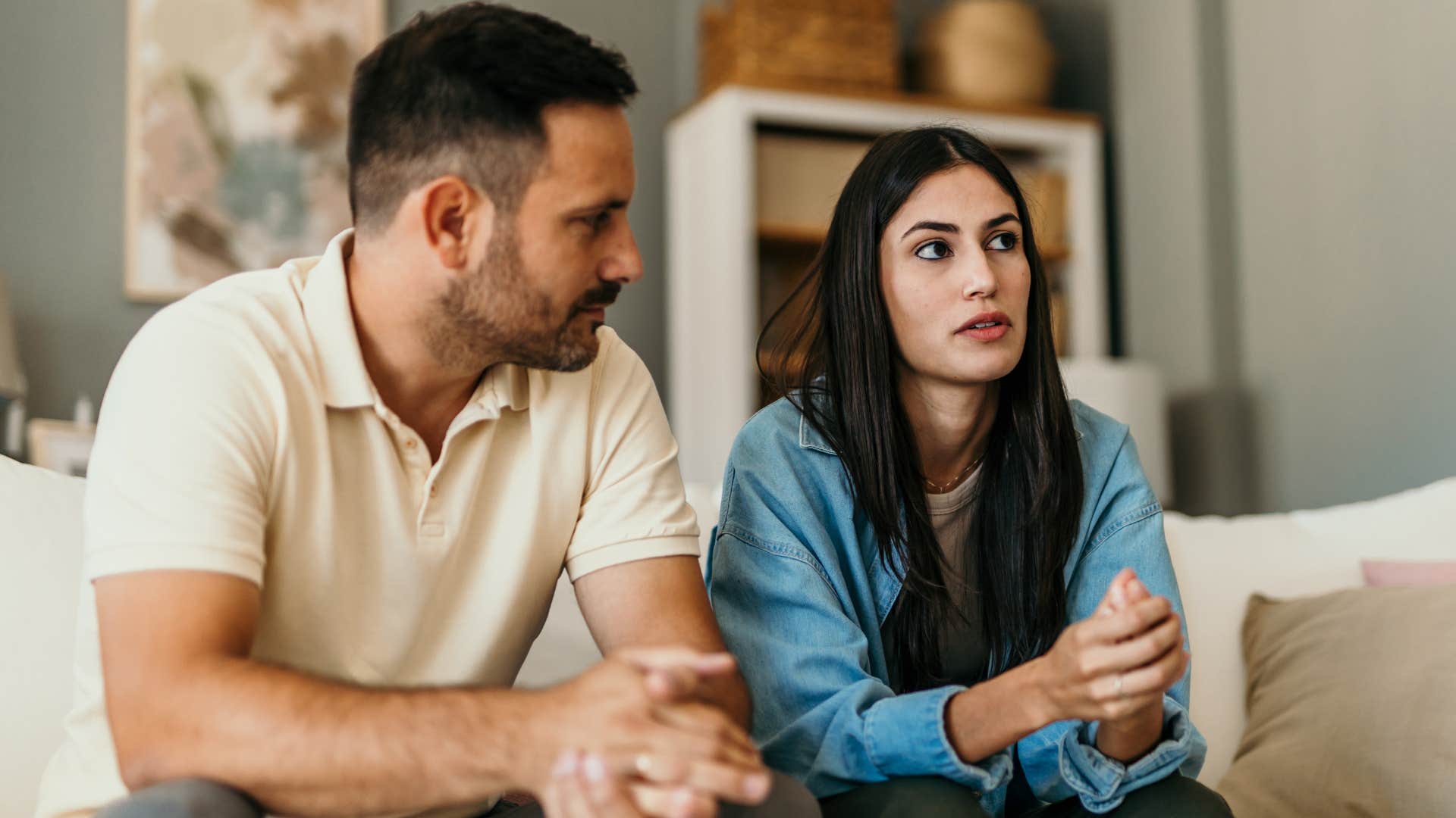 Woman looking upset sitting next to her husband on the couch.