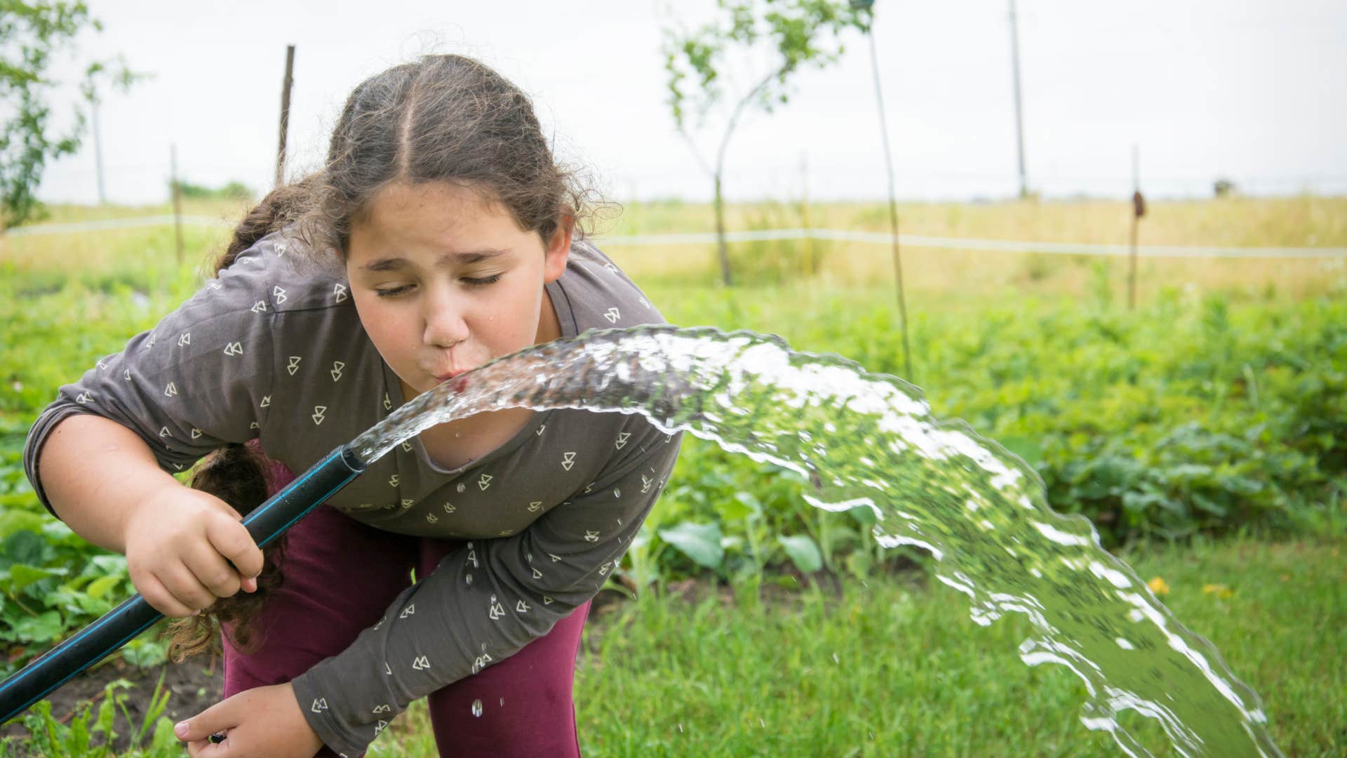 girl drinking water from a garden hose