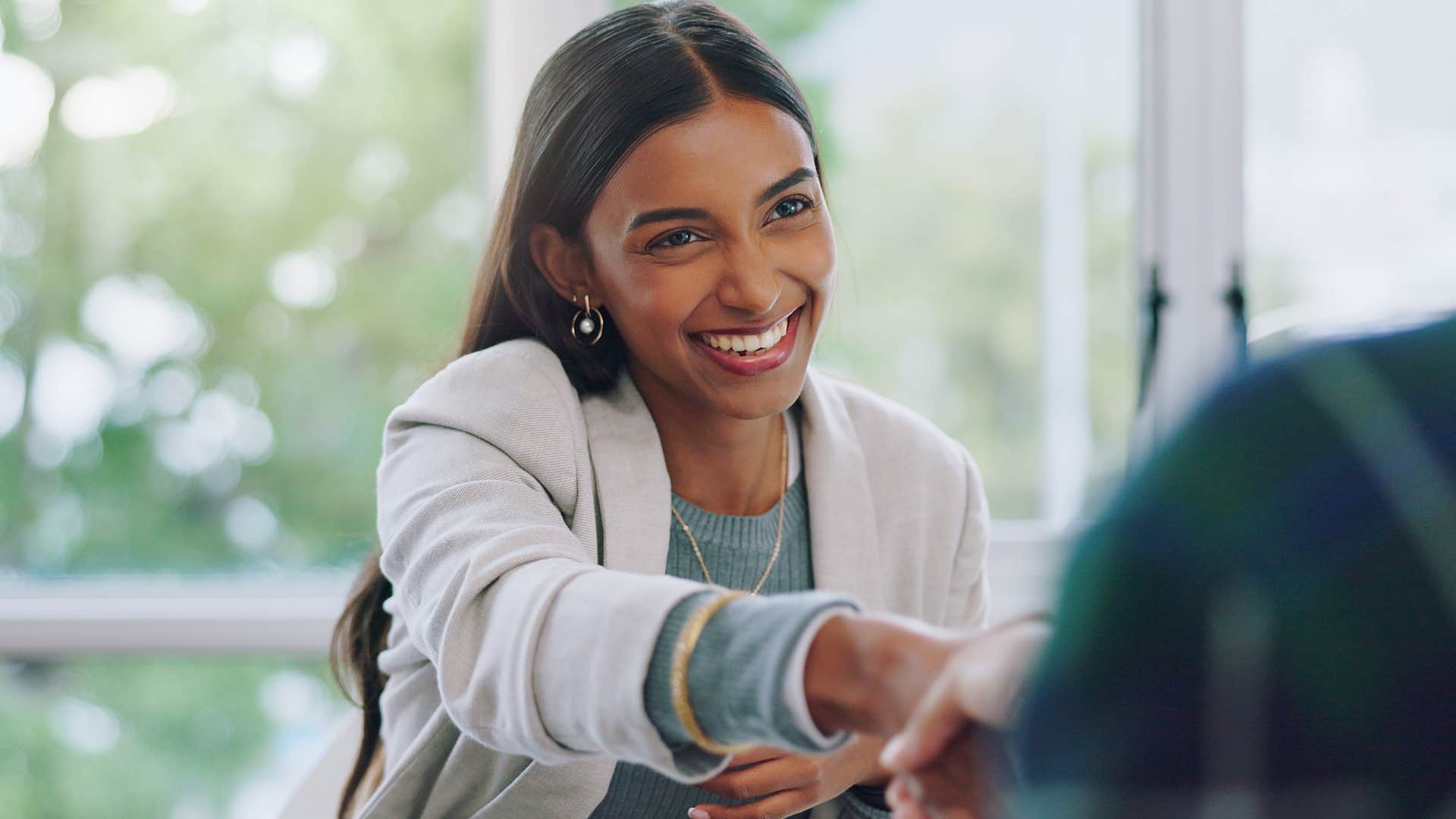 Woman smiling and shaking another person's hand. 