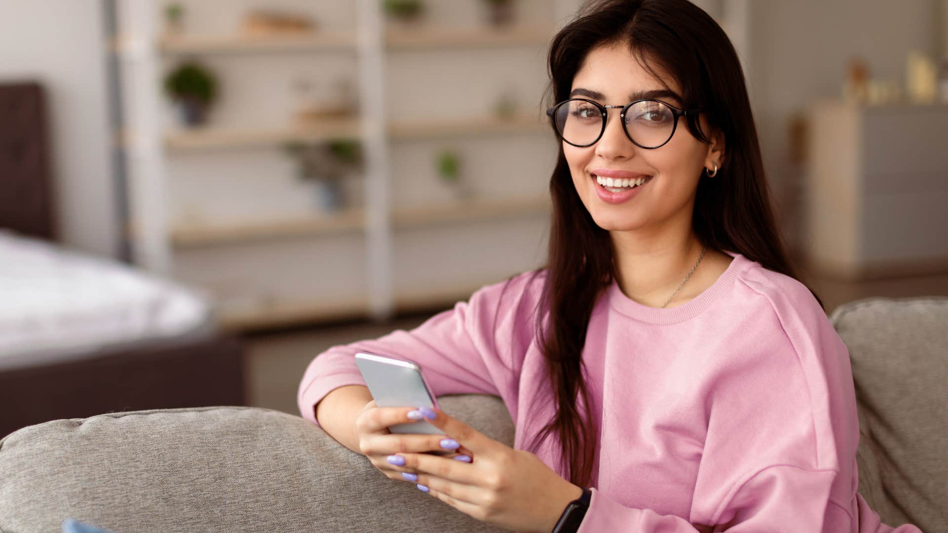 Young woman smiling on her phone while sitting on the couch.