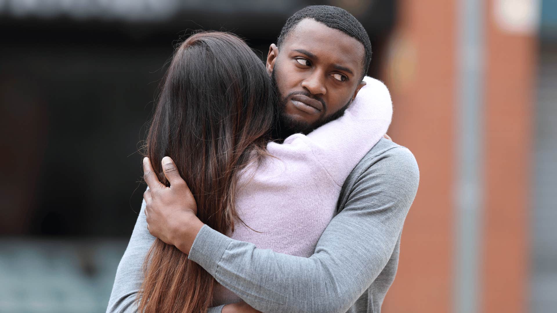 Man who is faking it rolls his eyes while hugging woman